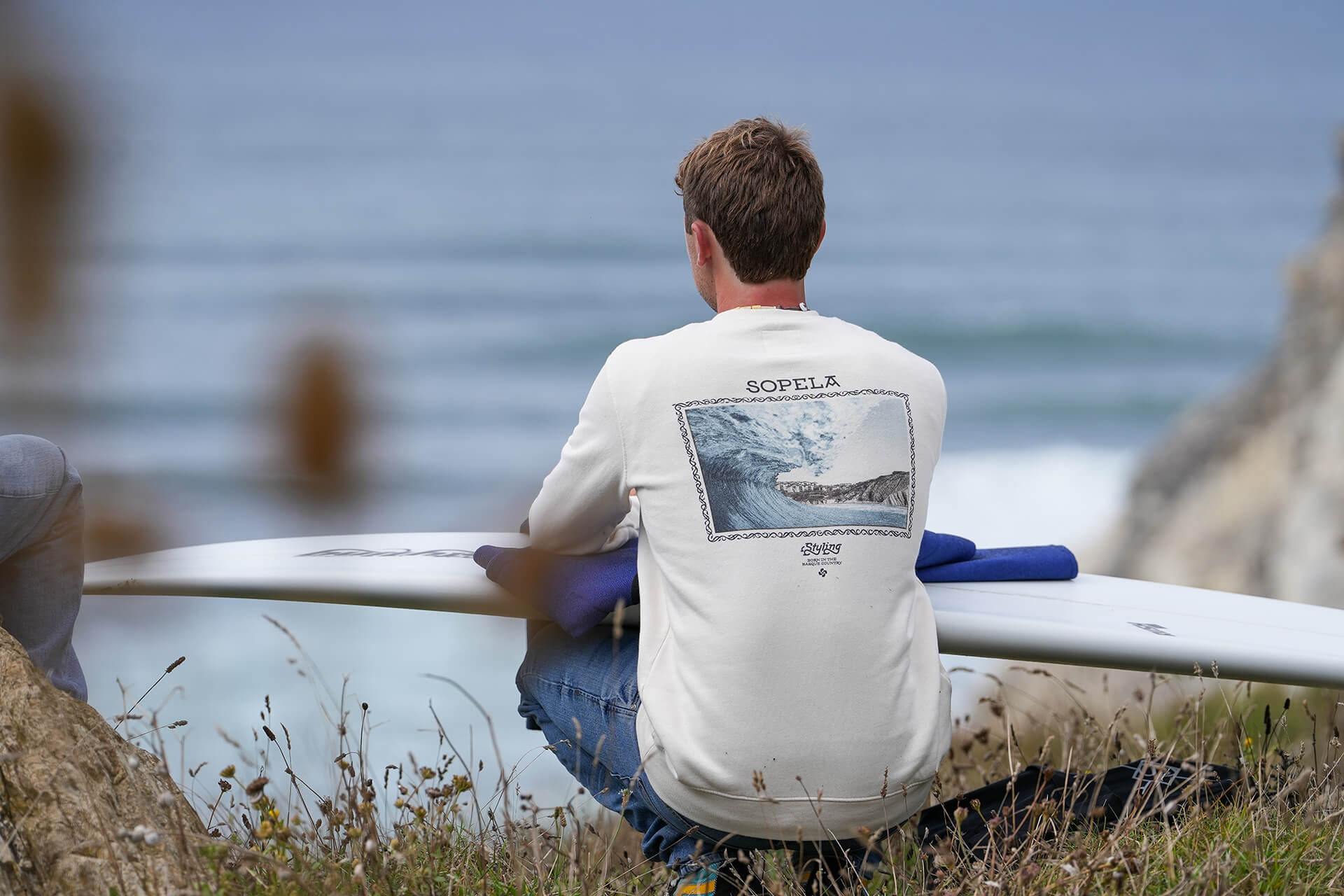 Un joven mirando al mar agachado con una tabla de surf en el regazo